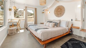 A bedroom with a bed, bedside tables, a chair, a hanging light fixture, and a view of the outdoors.