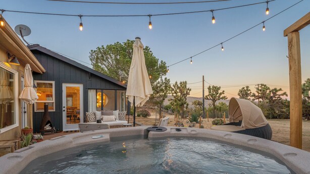 A hot tub area with a wooden deck, outdoor seating, and string lights.