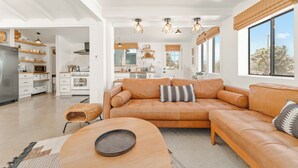 A spacious living area with a leather sofa, a round coffee table, and a kitchen in the background.