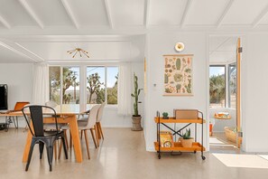 A spacious room with a dining area, a large window with a view of cacti, and a wall-mounted cactus-themed poster. - Le bungalow du désert: Amazing View, Spa, Cowboy Pool, Hike outside the backdoor (Yucca Valley)