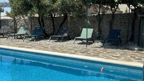 Ein Schwimmbecken mit klarem, blauem Wasser, umgeben von Steinmauern und grünen Liegestühlen.