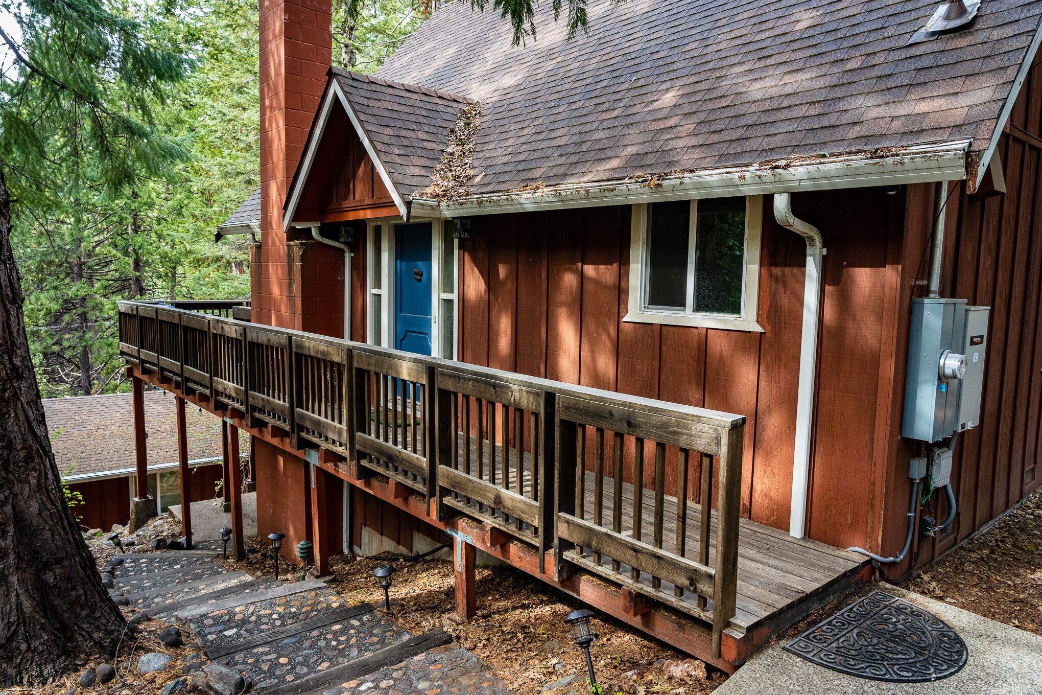 Une cabane en bois avec un porche, une porte bleue et une boîte électrique visible.