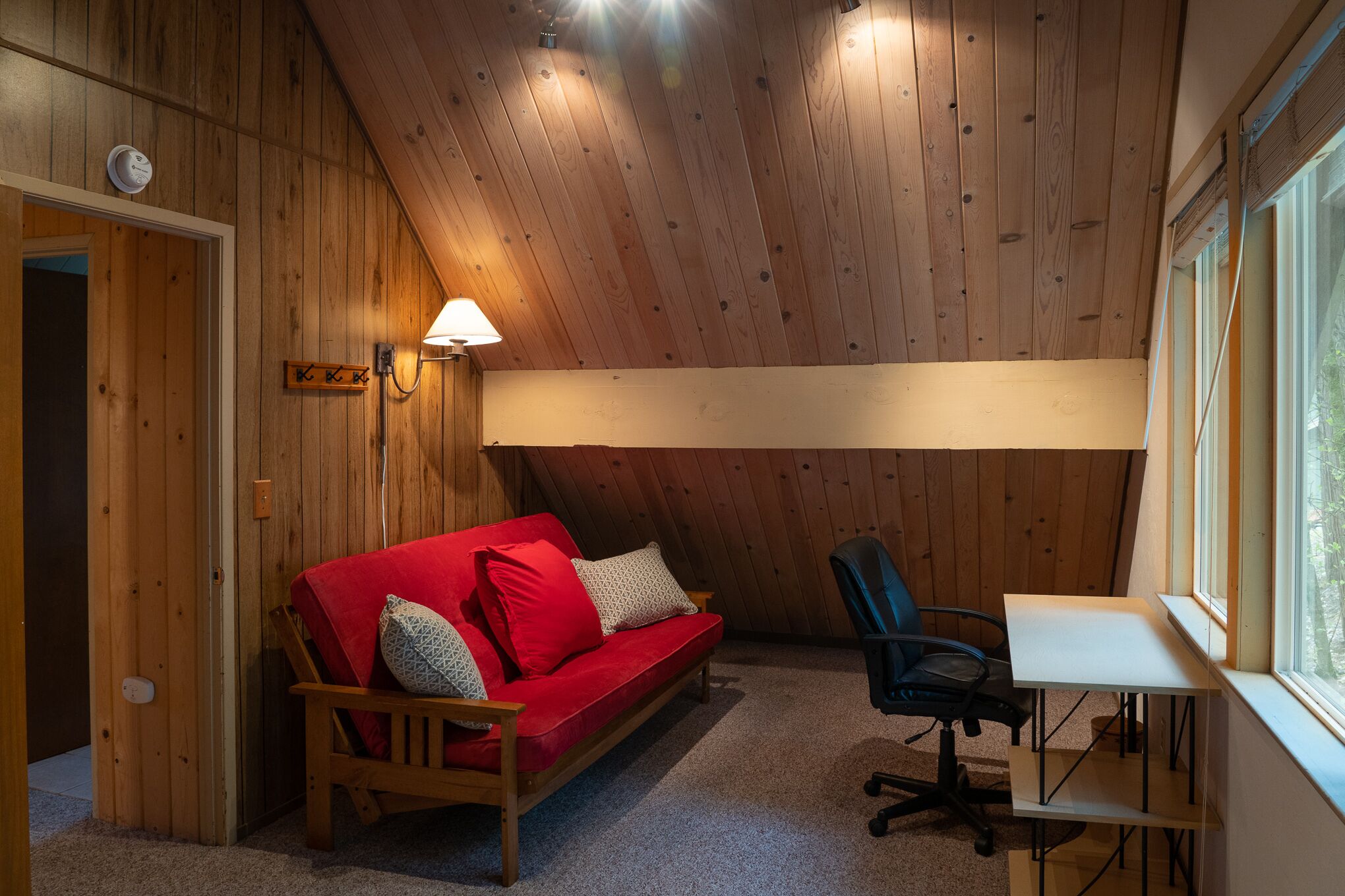 A cozy room with a wooden ceiling, a red sofa, a black office chair, and a small table.
