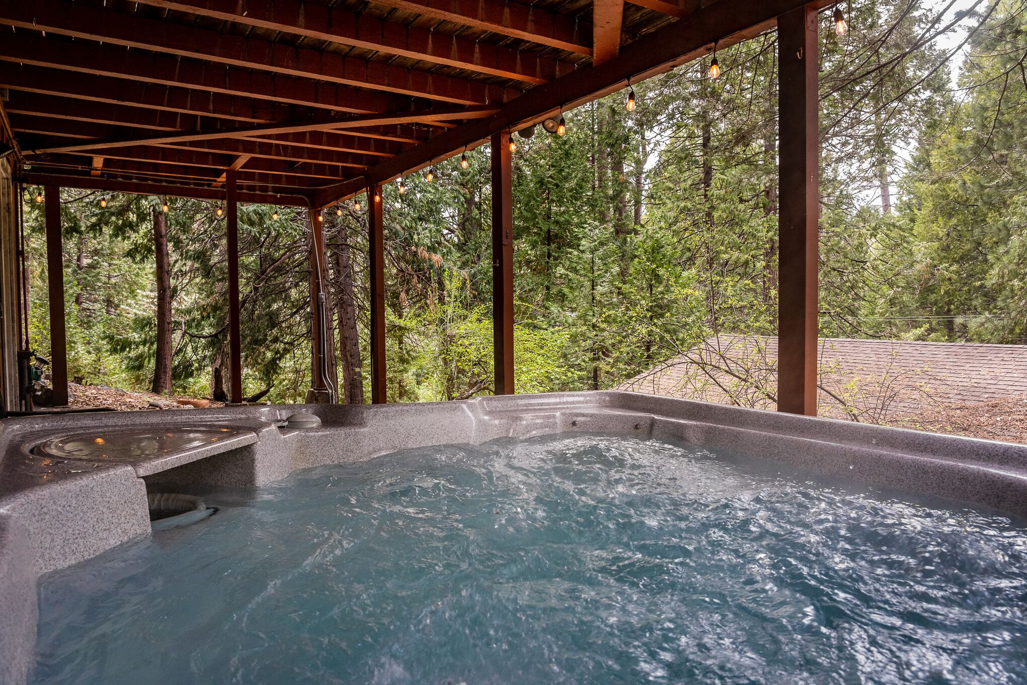 A hot tub under a wooden pergola with a forest view.