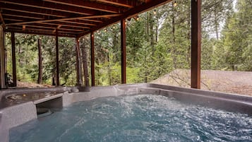 A hot tub under a wooden pergola with a forest view.