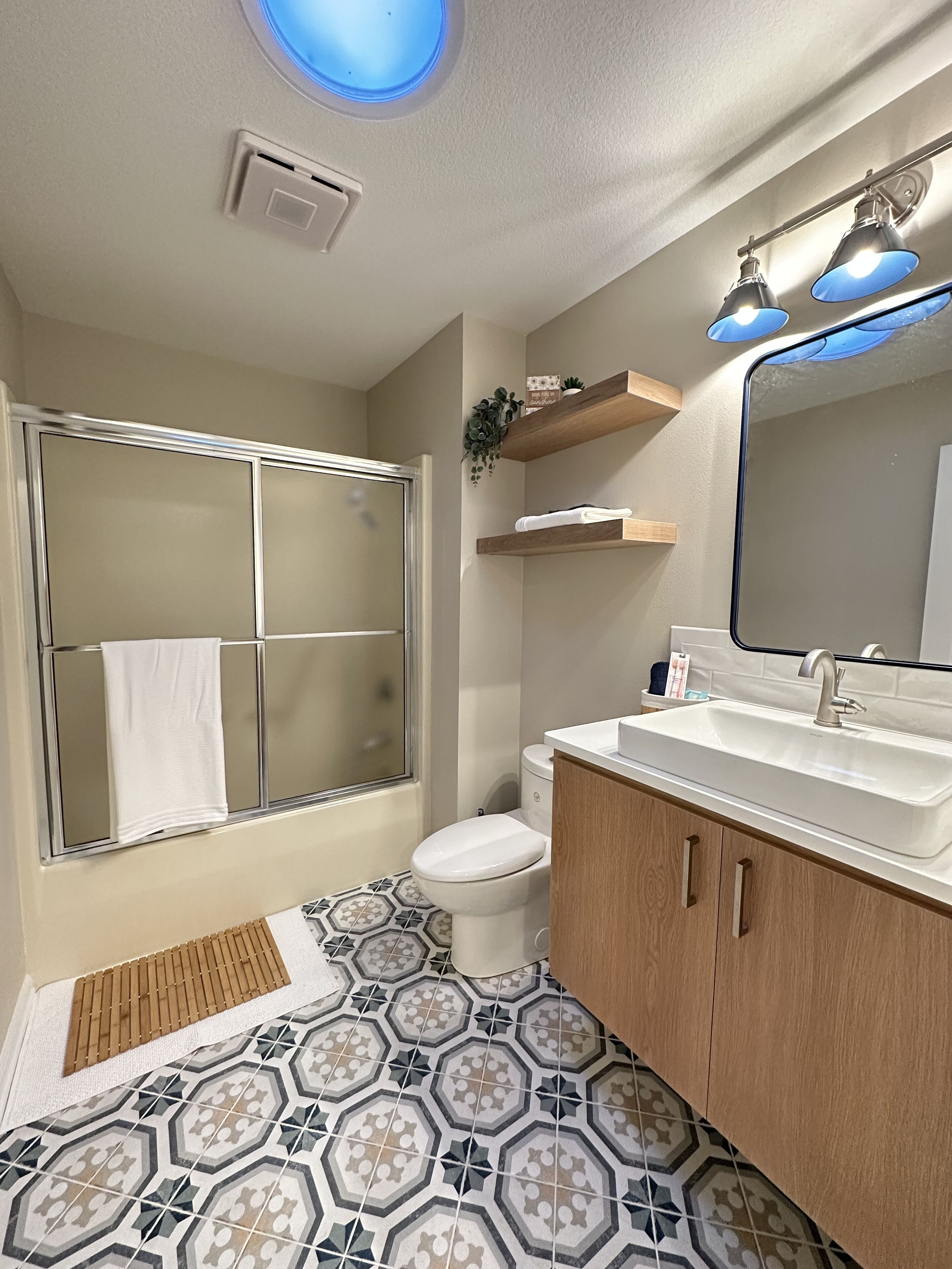 A bathroom with a shower, toilet, sink, and mirror.