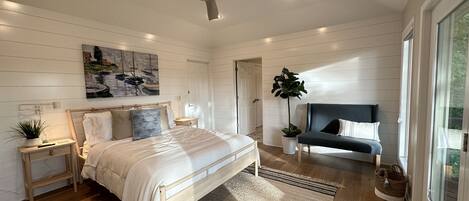 A bedroom with a bed, bedside tables, a nightstand, a window, a plant, and a ceiling fan.