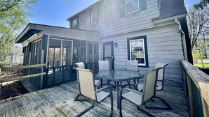 A covered patio with a glass enclosure, a table with chairs, and a wooden deck.