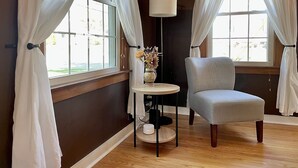 A room with a light grey armchair, a small round table with a vase of flowers, and a floor lamp.