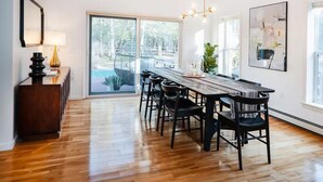 A spacious dining area with a long wooden table, black chairs, and a modern chandelier.