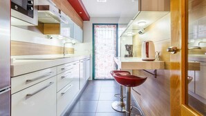 Een moderne keuken met witte kasten, roestvrijstalen apparatuur en een rode barkruk.