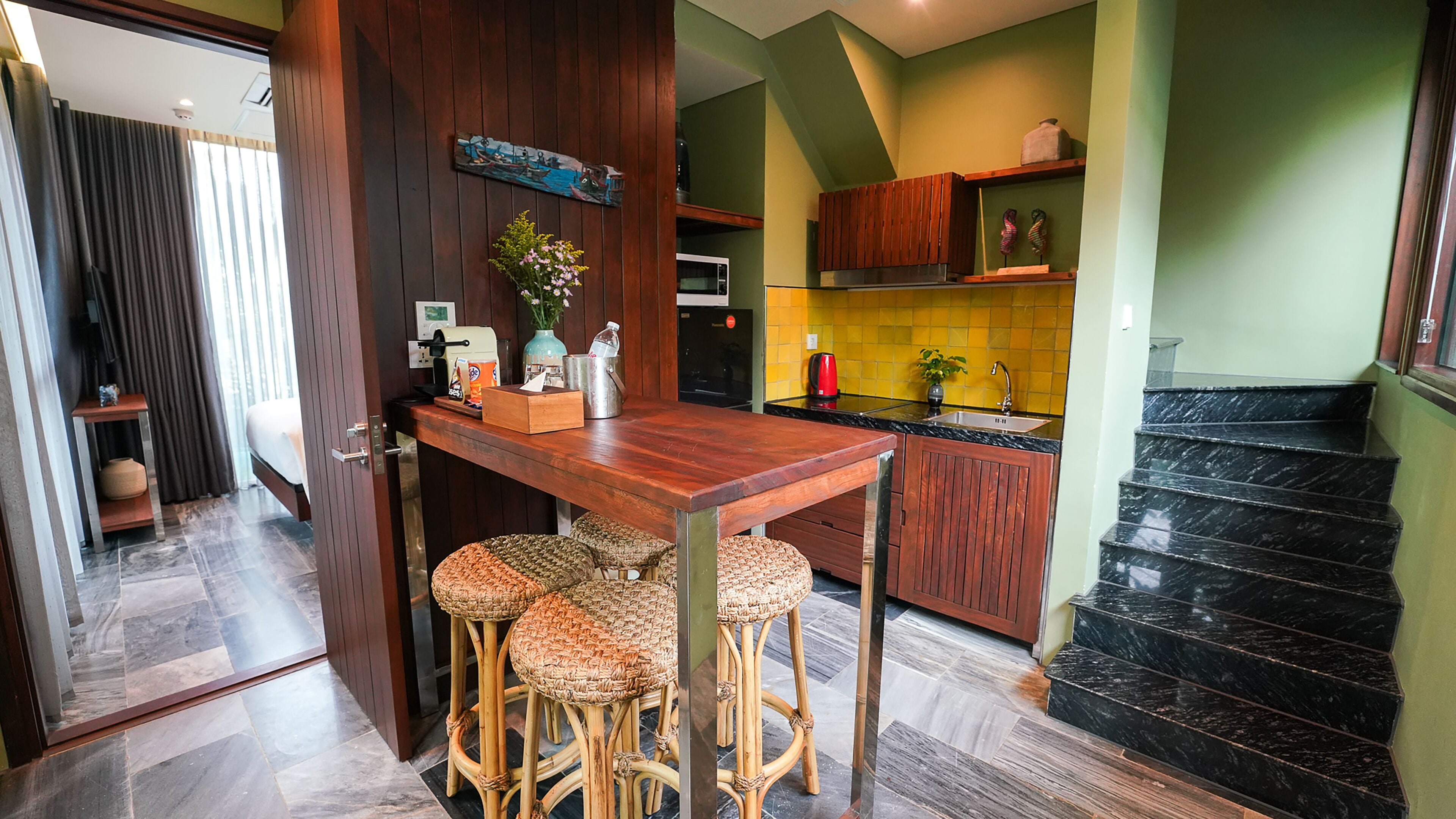 A modern kitchen with a wooden bar, wicker stools, and a dining table.
