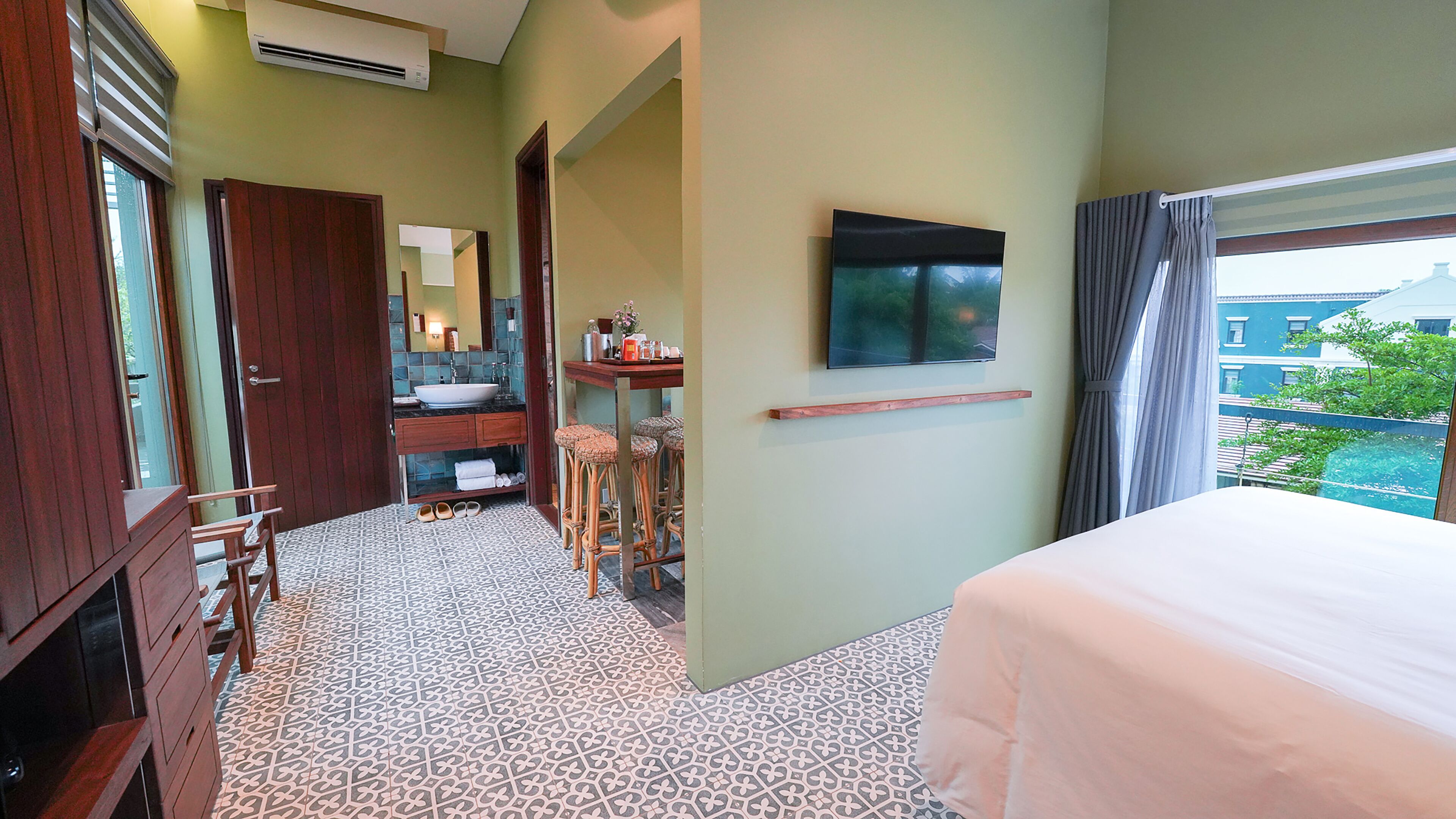 A hotel room with a bed, a bathroom with a sink and mirror, a small table with chairs, and a TV on the wall.