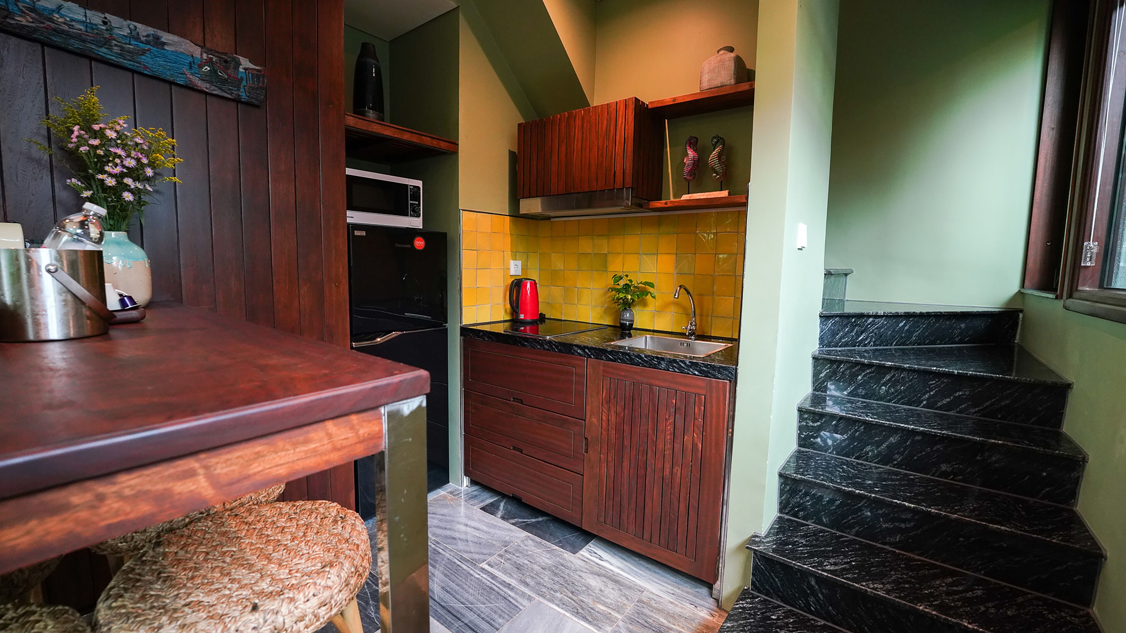 Een keuken met houten kastjes, een magnetron, een spoelbak en een trap naar een ander niveau.