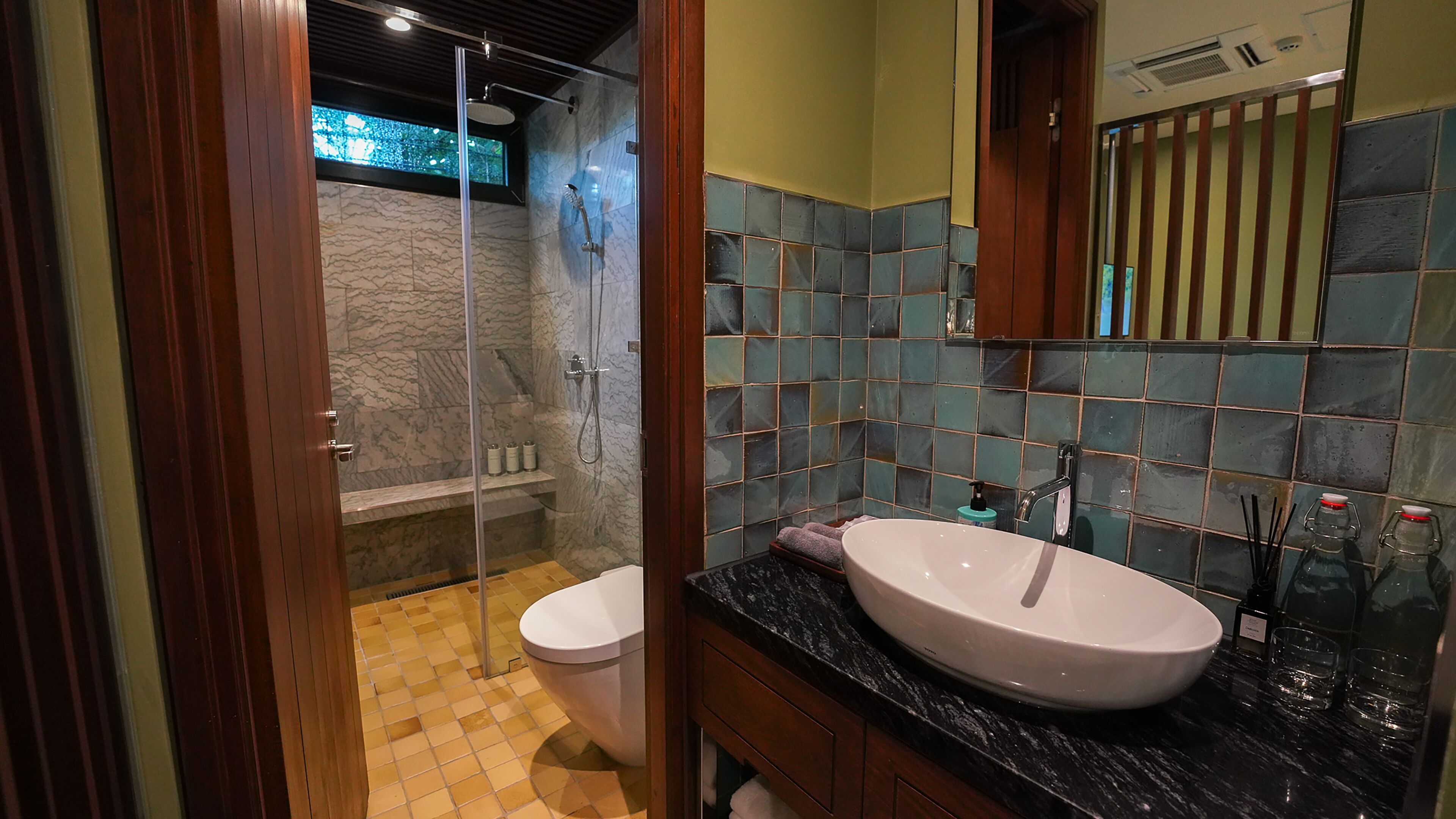 A bathroom with a glass-enclosed shower, a white toilet, a sink with a black countertop, and a tiled wall with a mirror above it.