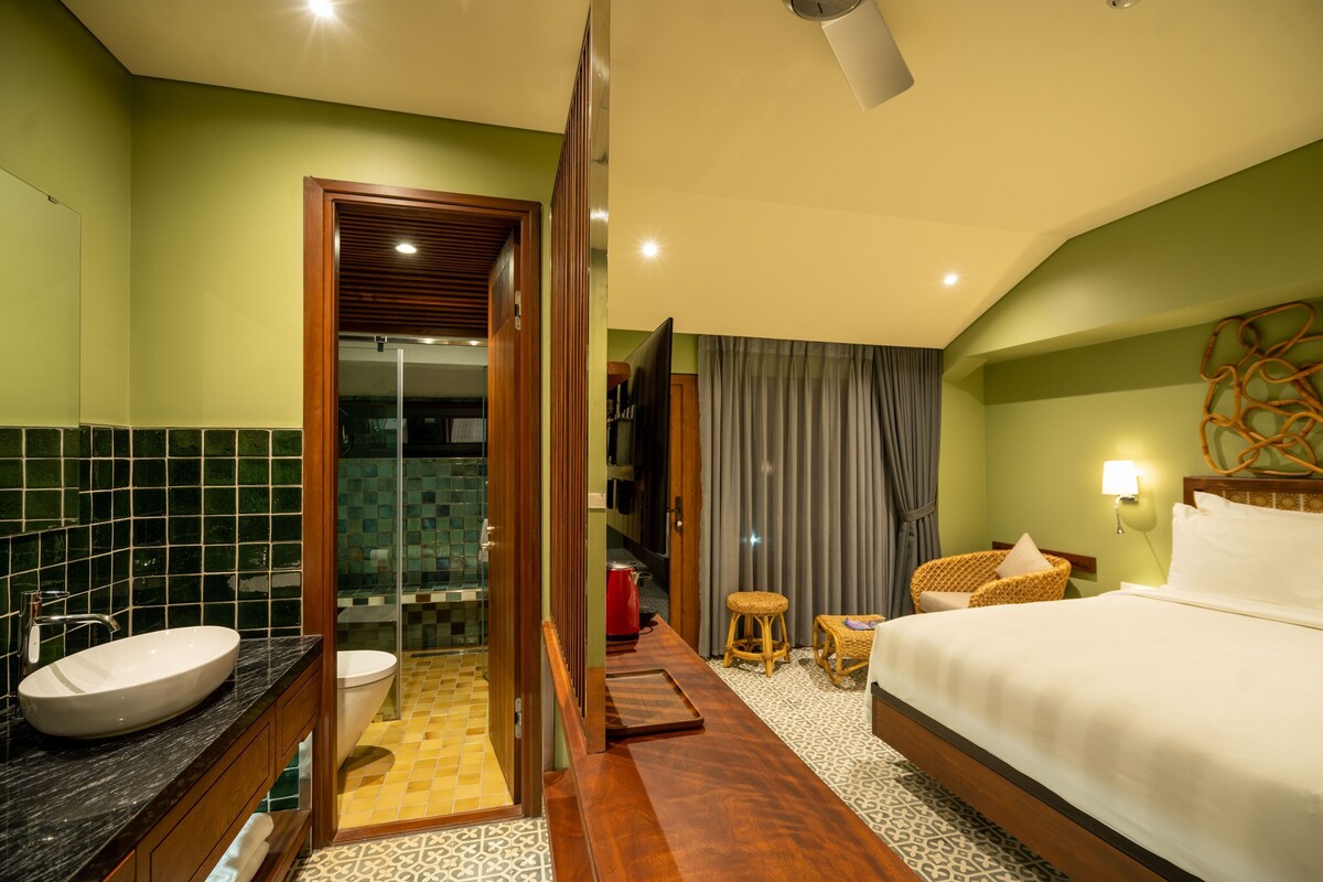 A hotel room with a bathroom, a bed, a sitting area, and a shower.
