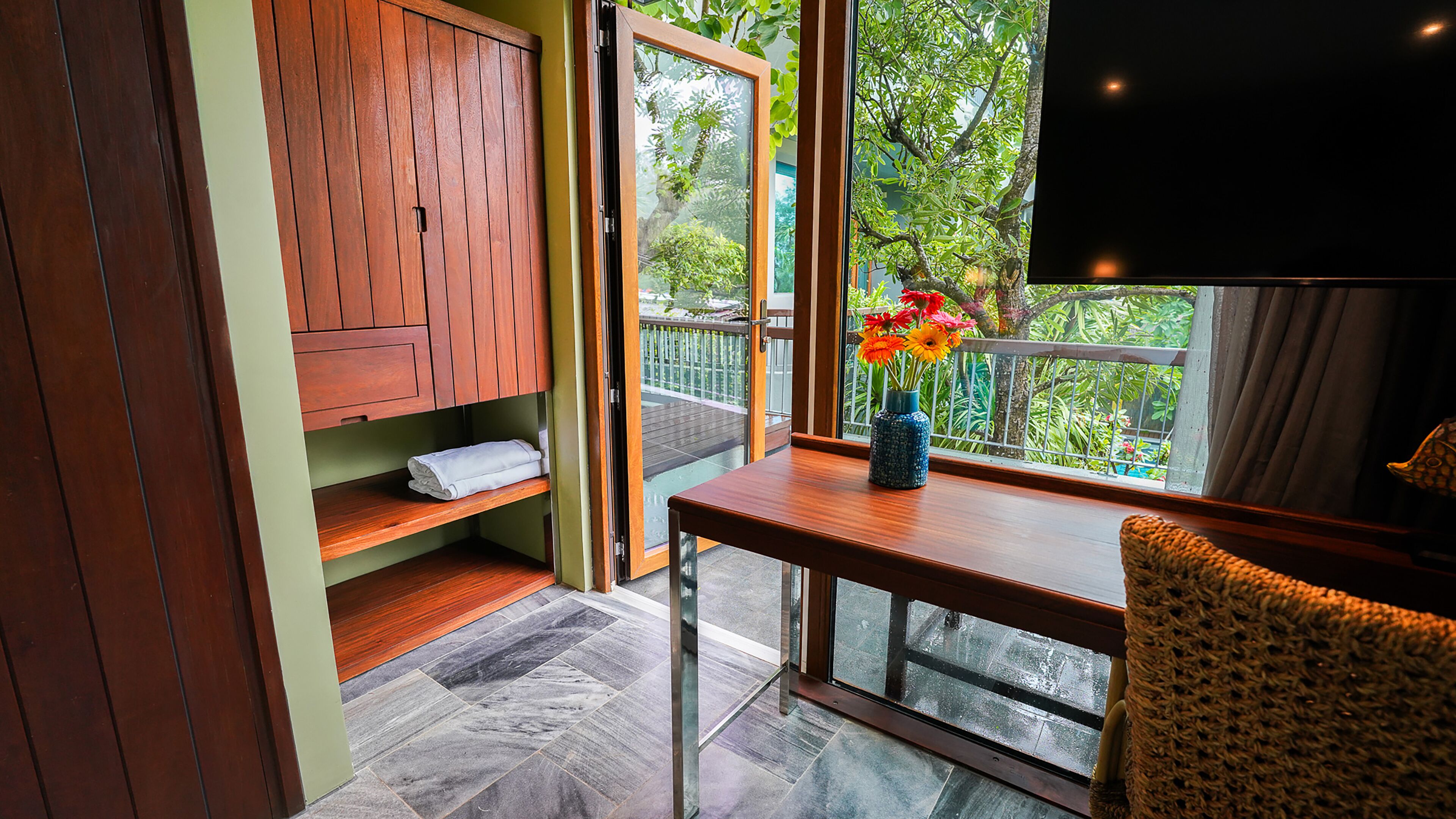 Una habitación con un armario de madera, una mesita con un jarrón de flores y vistas a zonas verdes.