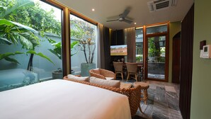 A hotel room with a large bed, wicker furniture, a TV, and a view of greenery outside. - Hotel Chiem Hoian (Da Nang)