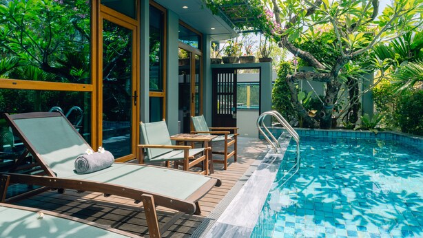 A poolside area with lounge chairs, a small table, and a glass-enclosed room with a view of the pool. - Hotel Chiem Hoian (Da Nang)