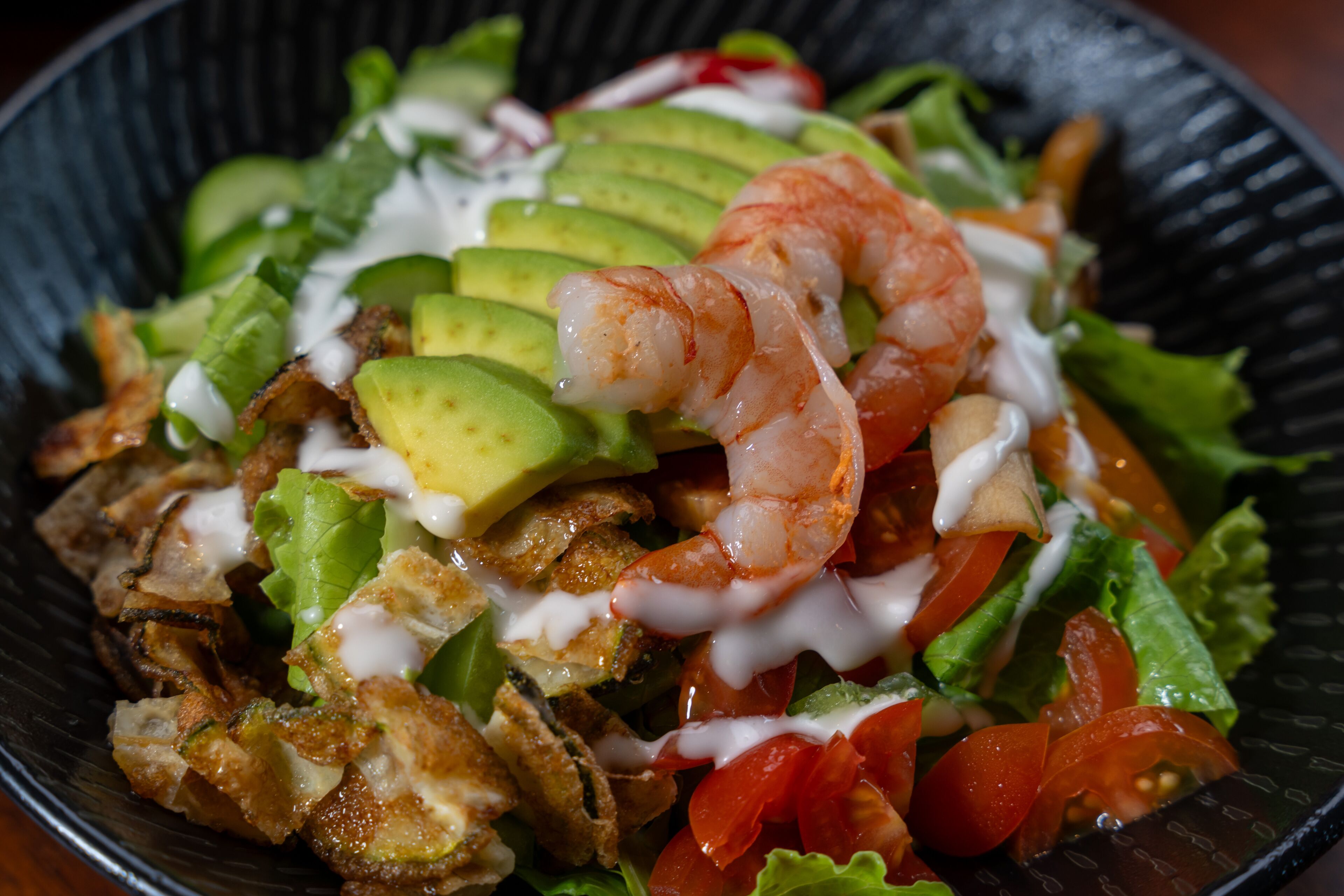 A salad with shrimp, avocado, and various vegetables in a bowl.