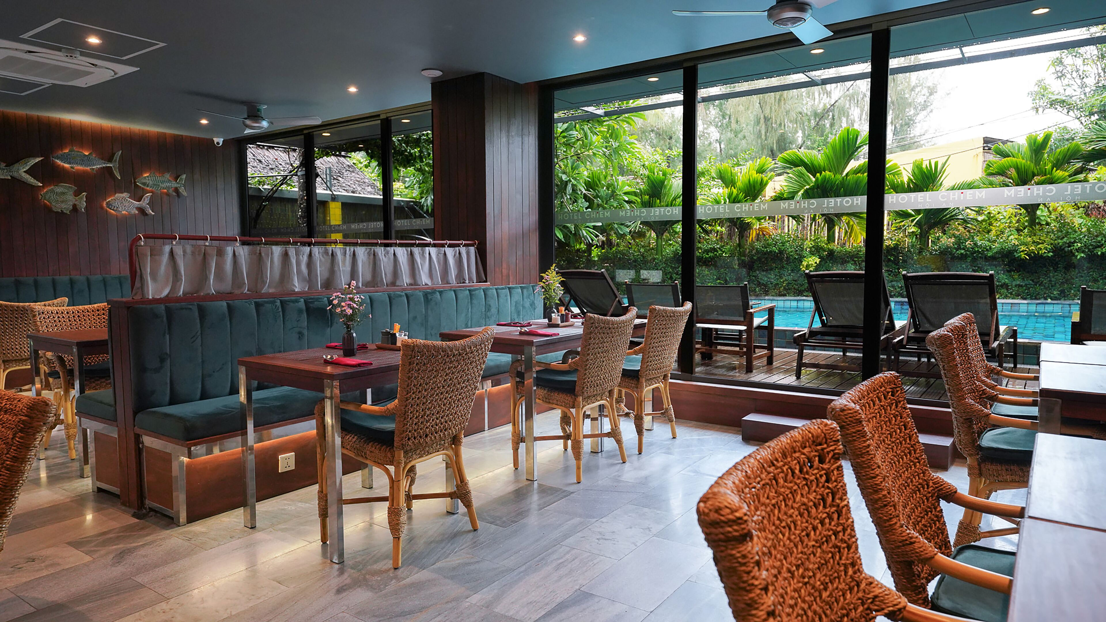 A restaurant with a pool view, wooden furniture, and a green cushioned seating area.
