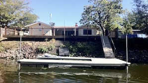 Une maison avec une jetée qui s’avance dans l’eau, entourée d’arbres et d’une petite colline.