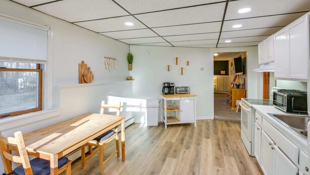 Cocina compacta con muebles blancos, una mesa de comedor de madera y un refrigerador pequeño blanco.