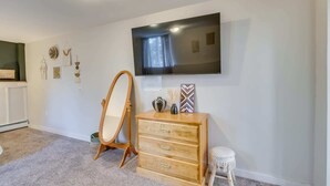 Un dormitorio con un aparador de madera, un taburete pequeño, un espejo y un televisor de pantalla plana montado en la pared.