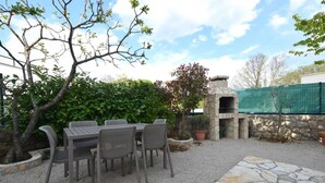 An outdoor patio with a stone table and chairs, a stone oven, and a green fence. - Apartment Letizia with two bedrooms (Rasopasno)