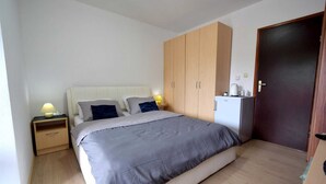 A bedroom with a bed, two bedside tables, a wardrobe, a door, and a refrigerator. - Apartment Letizia with two bedrooms (Rasopasno)