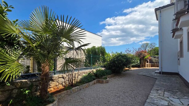 A gravel driveway leading to a white building with a stone wall and a palm tree. - Apartment Letizia with two bedrooms (Rasopasno)