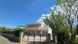 A two-story house with a gated entrance, a driveway, and a tree in the foreground. - Apartment Letizia with two bedrooms (Rasopasno)