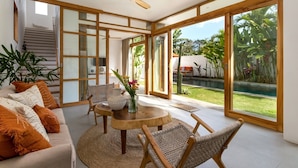 A spacious living area with a sofa, chairs, a coffee table, and a view of a pool and garden.