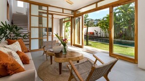 Ampla sala de estar com sofá, cadeiras, mesa de centro e vista para a piscina e jardim.