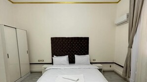 A neatly arranged bedroom with a large bed, a chandelier, an air conditioning unit, and a wardrobe. - Palace Court (Cairo)