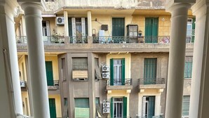 A balcony with two chairs and a table, marble flooring, and a view of multi-story buildings with balconies. - Palace Court (Cairo)
