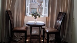 A room with a wooden floor, two chairs, a small table with a vase of flowers, and a window with curtains. - Palace Court (Cairo)
