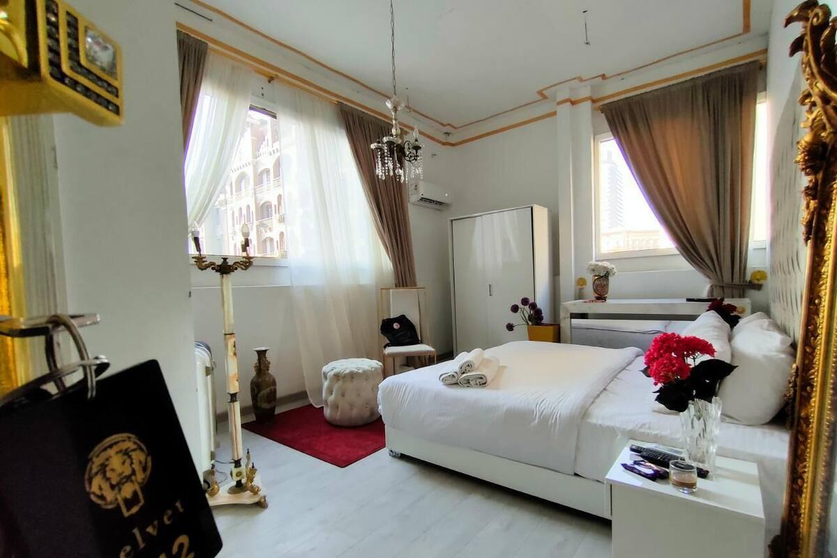 A modern hotel room with a large bed, a bedside table, a wardrobe, and a window with curtains.