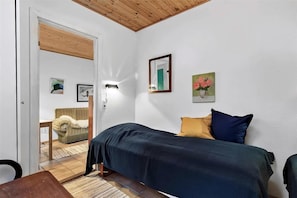A bedroom with a bed, a chair, a table, and a door leading to another room.