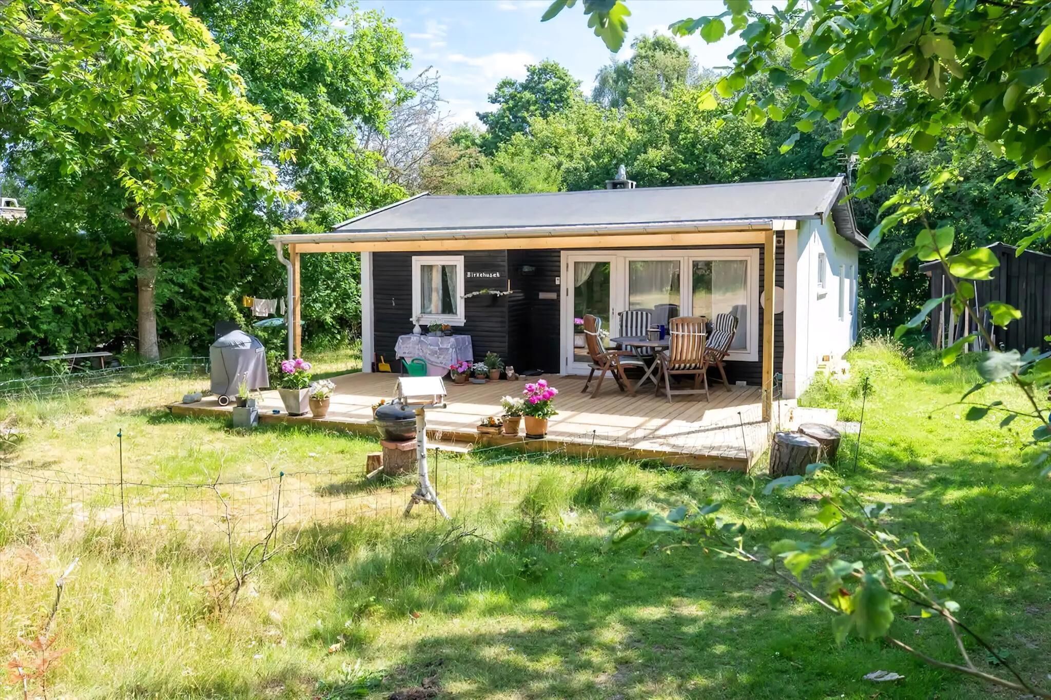 Ein kleines Haus mit Terrasse, überdachter Veranda und einem Garten mit Blumentöpfen.