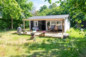 Ein kleines Haus mit Terrasse, überdachter Veranda und einem Garten mit Blumentöpfen.