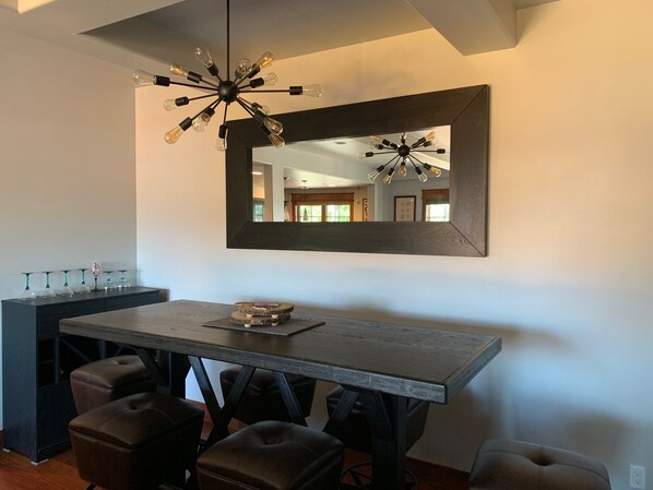 Un coin repas comprenant une grande table, plusieurs chaises, un luminaire suspendu et un miroir au mur.