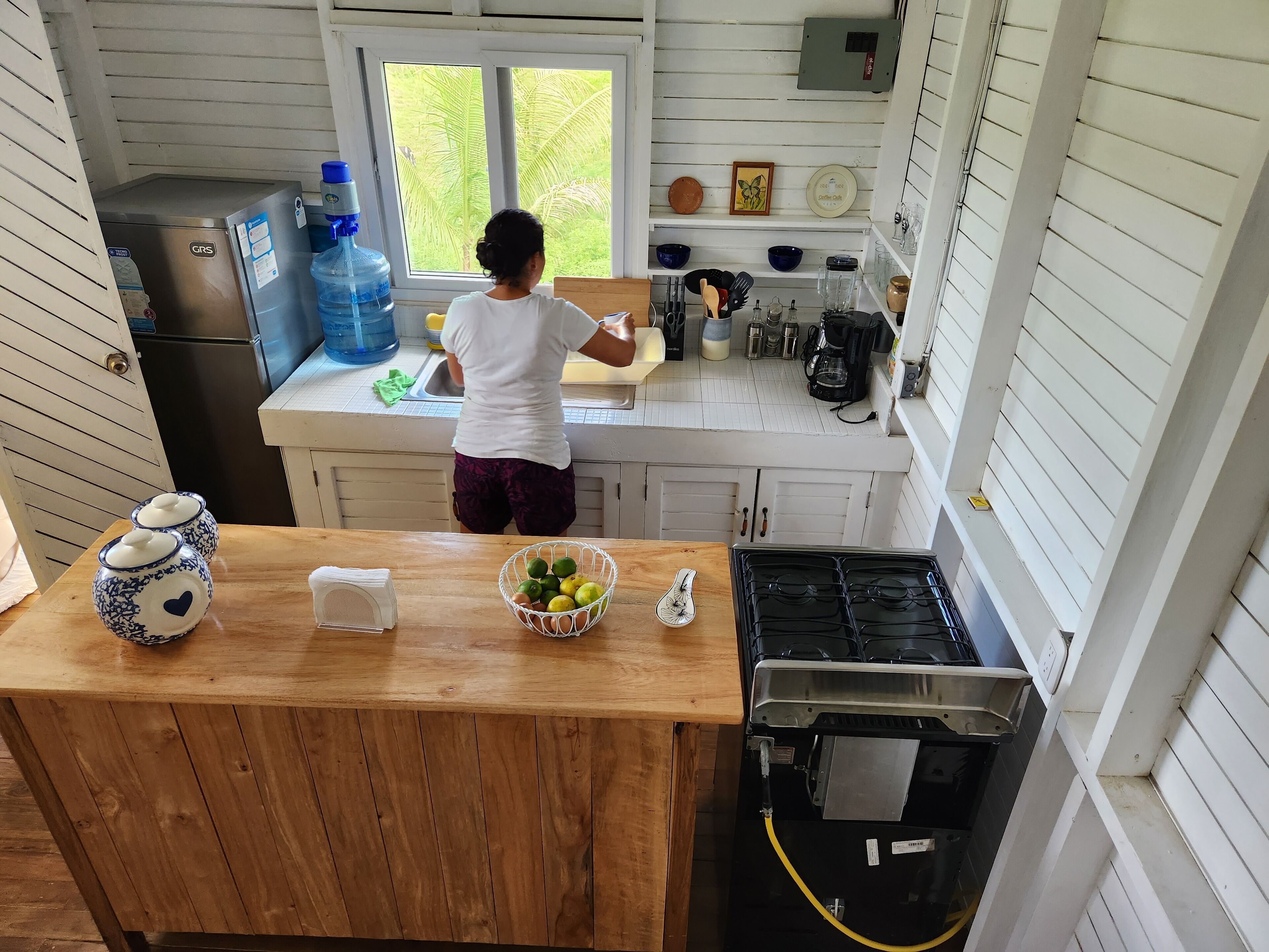 A kitchen with a large window, a refrigerator, a sink, and various kitchen items on the counter.