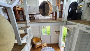 Een rustiek houten interieur met een eethoek, voorzien van een geruit tafelkleed, een rieten stoel en een hangende pot.