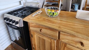 Een keuken met een gasfornuis, oven, houten keukenkastjes en een mand met fruit op het aanrecht.