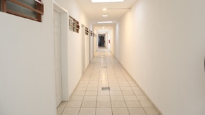 A long, narrow hallway with white walls and tiled flooring, leading to a door at the end. - Hostal Purísima (Purísima del Rincón)