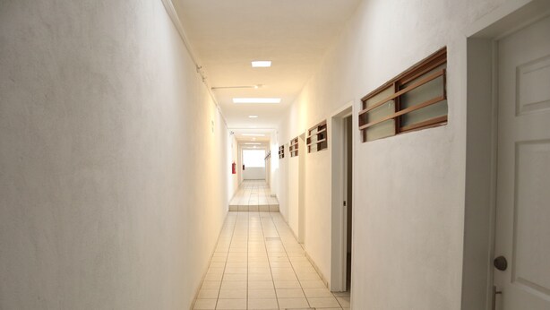 A long, narrow hallway with white walls and a tiled floor, leading to a door at the end. - Hostal Purísima (Purísima del Rincón)