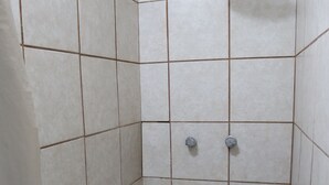 A small, tiled shower stall with a showerhead and two faucets. - Hostal Purísima (Purísima del Rincón)