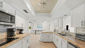A modern kitchen with white cabinetry, a stainless steel microwave, and a coffee maker. - Bayside Retreat with Backyard Oasis (Tampa)