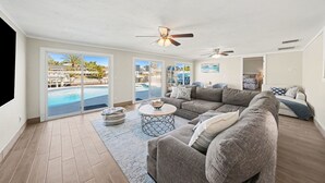 A spacious living room with a large sectional sofa, a round coffee table, and a view of a swimming pool through large sliding glass doors. - Bayside Retreat with Backyard Oasis (Tampa)